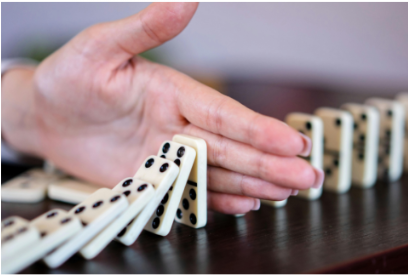 eine Frauenhand stoppt eine Reihe umfallender Dominospielsteine